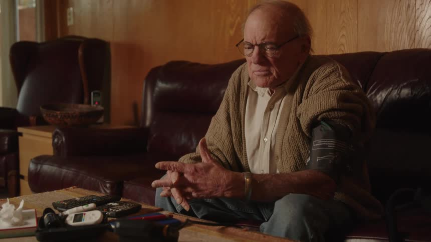 Elderly man sitting on a couch at home takes his blood pressure with a machine