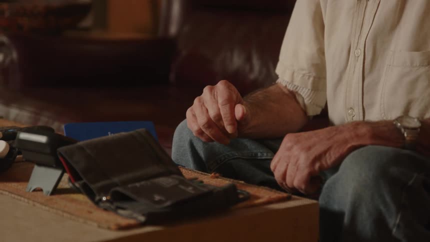 Elderly man sitting on a couch at home hesitantly grabs a blood pressure machine from the coffee table