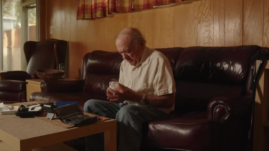 Elderly man sitting in a comfortable leather couch at home cleans his glasses