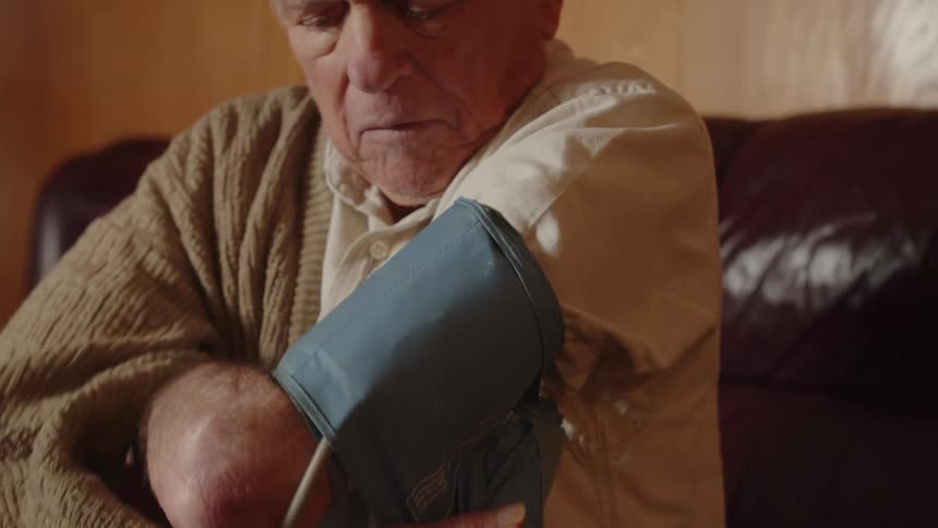 An old elderly man is sitting down and taking his blood pressure