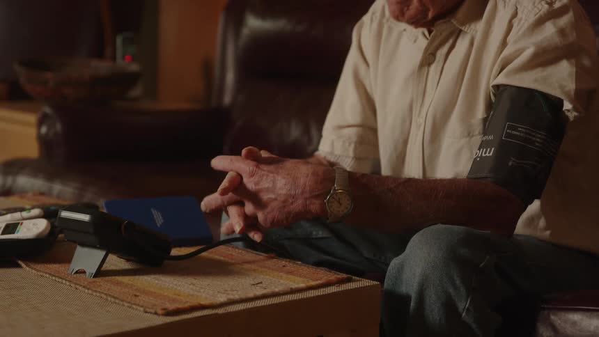 Elderly man uses blood pressure machine at home and writes down reading