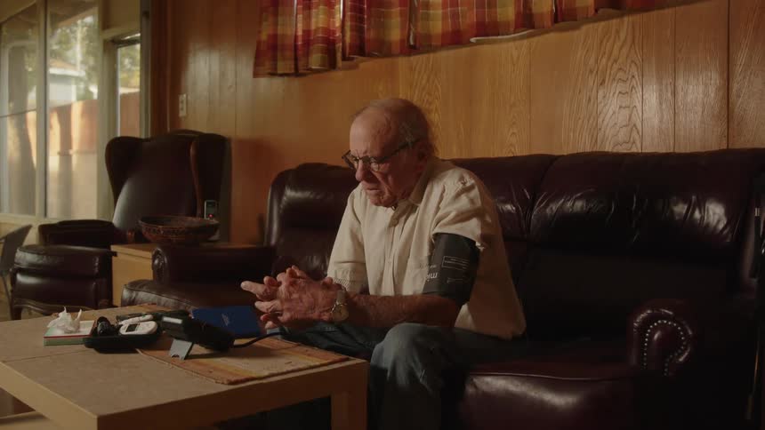 Elderly man sitting on a couch at home takes his blood pressure with a machine
