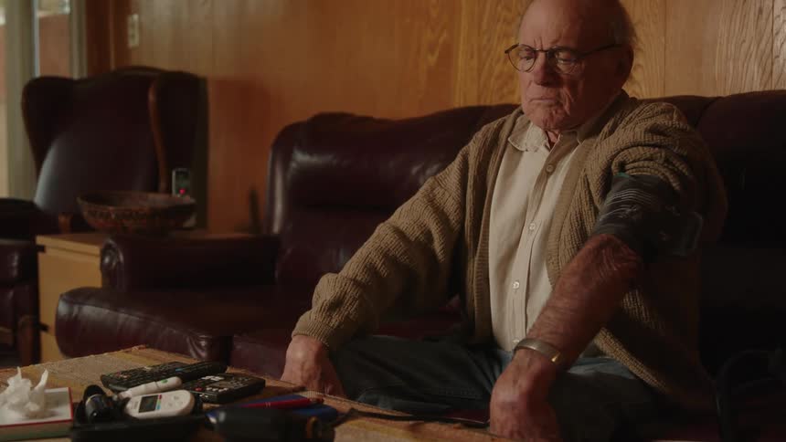 An older elderly man is sitting down on a couch indoors