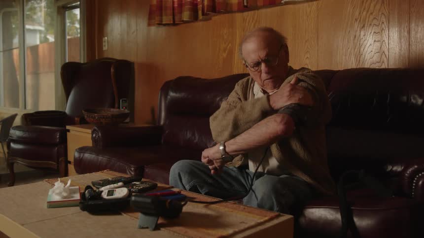 A man is sitting on his living room couch wrapping a blood pressure cuff around his arm