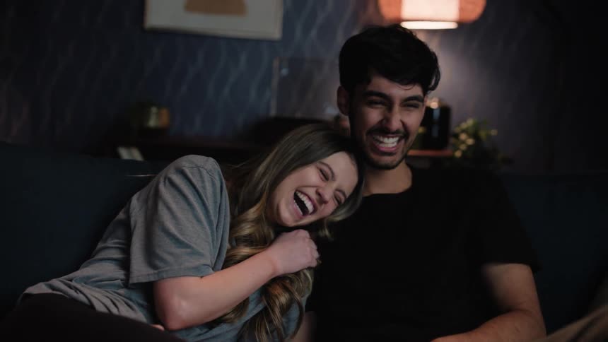 Young happy couple sitting together on the couch at home watching television