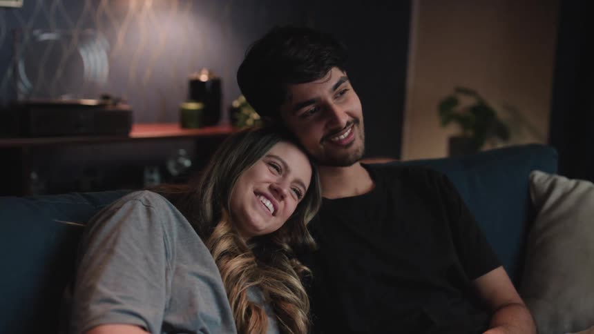 Young happy couple sitting together on the couch at home watching television