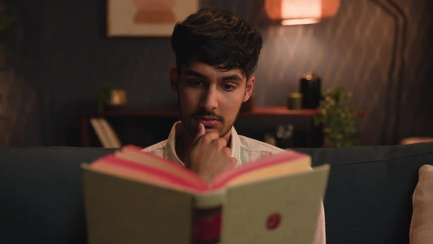 A young man is reading a book inside of his home