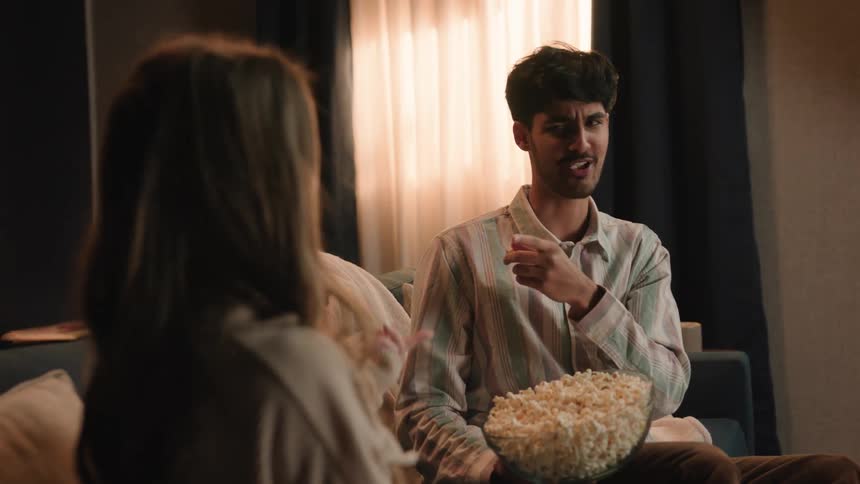 Young couple is sitting on the couch and eating some popcorn