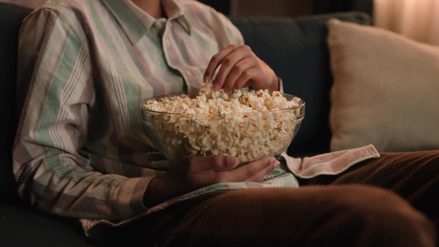 A person sits on their couch eating popcorn out of a bowl