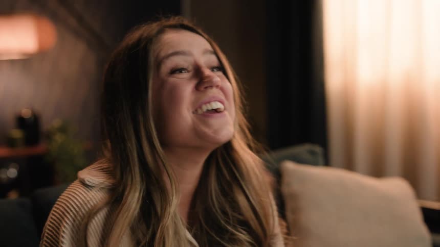 Young attractive woman sitting in the living room covers her mouth while laughing