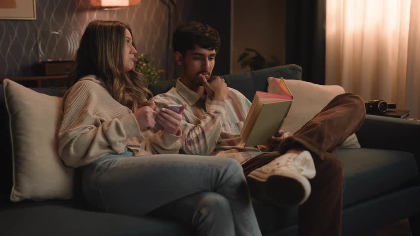 Woman trying to show something on phone to reading man pouts until he pays attention