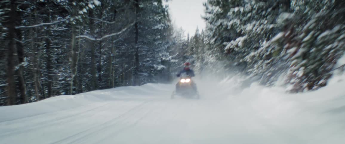 Snowmobile coming down powdery ski run during the day
