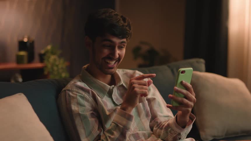 Man laughs and gestures while sitting on couch during a video call