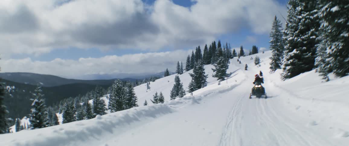 People move along track filled snowy path on mountain in snowmobiles