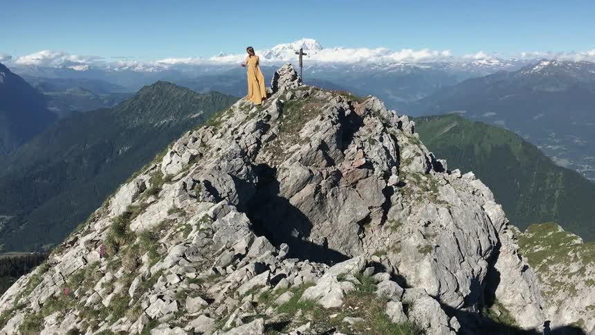 A woman in a yellow dress stands on a rocky hill