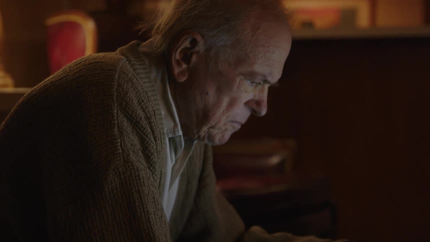 An older elderly man is sitting down and is on his laptop