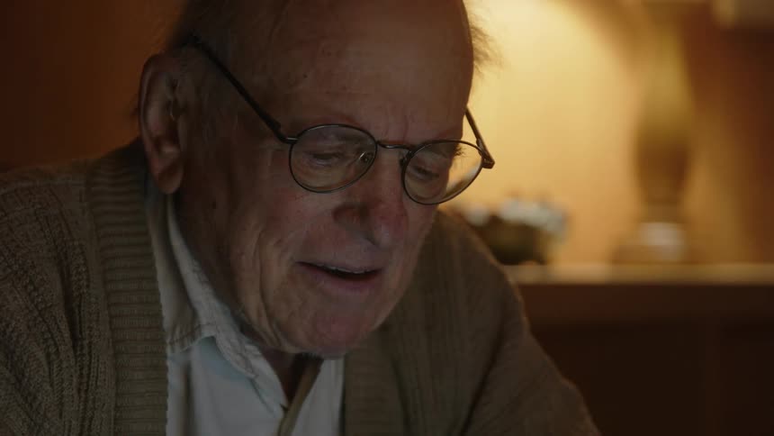 An elderly man is sitting down and works on his laptop