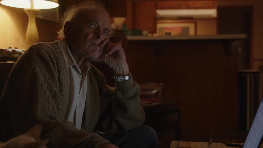An older elderly man is sitting down and is on his laptop