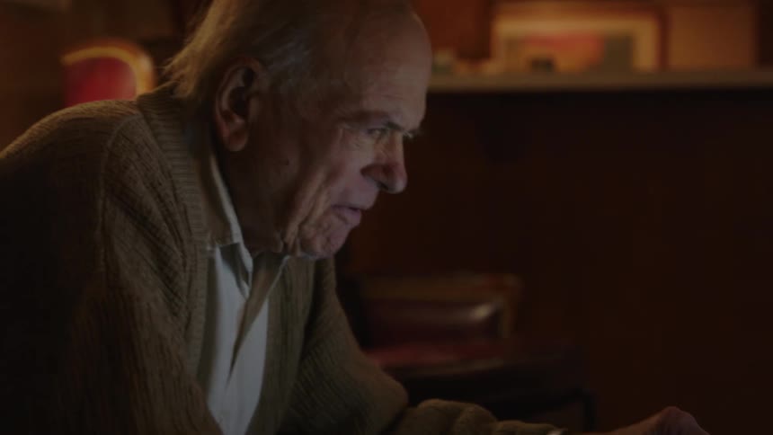 Elderly man sitting on a couch at home types on a laptop over the coffee table