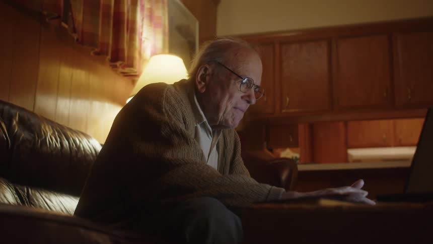 A elderly man is typing on his laptop