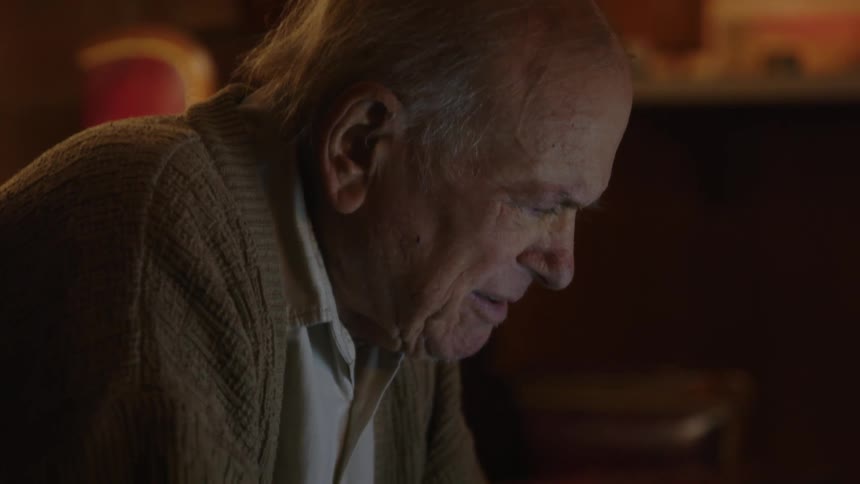 An older elderly man is sitting down and is on his laptop