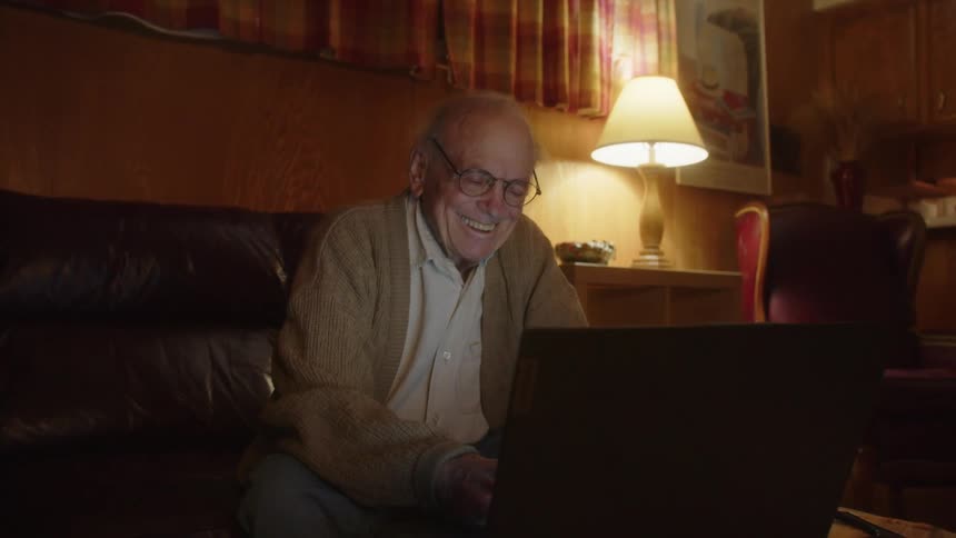 A man is laughing while using his laptop