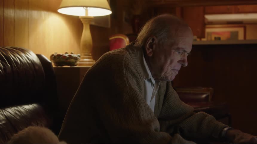 An older elderly man is sitting down and is on his laptop