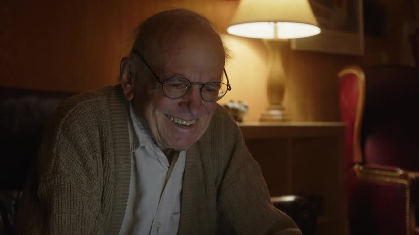 A man is sitting at a table in front of a laptop computer smiling and laughing as he types on the keyboard