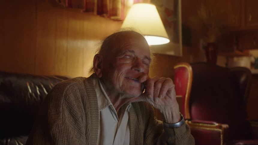 Happy elderly man sitting on a couch at home looks up while having fond memories
