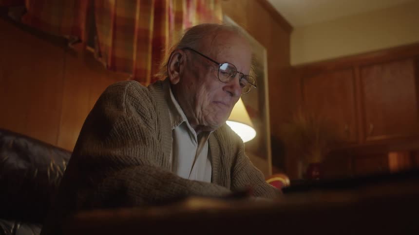 Elderly man smiles and puts on eyeglasses before typing on laptop