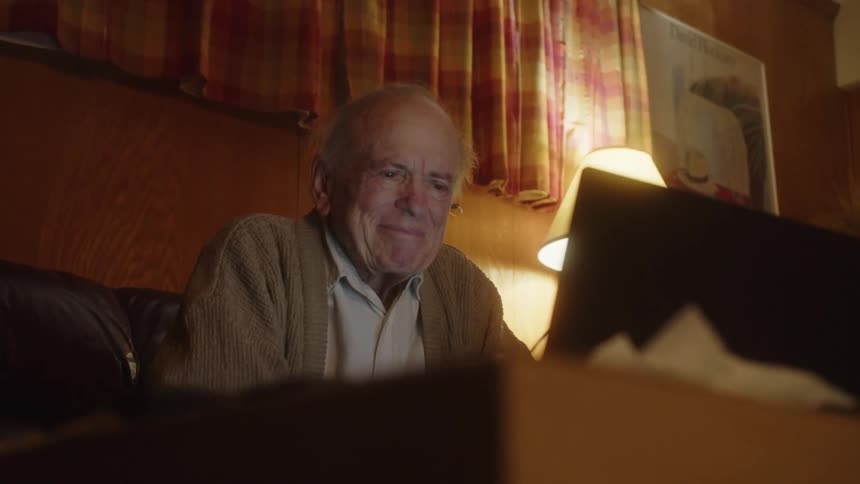 Elderly man thinks before putting on his eyeglasses and typing on laptop