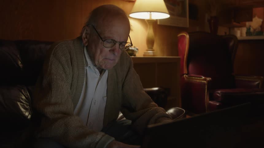A man is sitting in his living room typing on a laptop computer