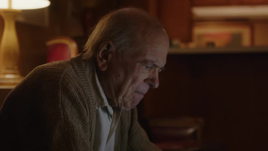 Elderly man sitting in living room thinks before continuing to type