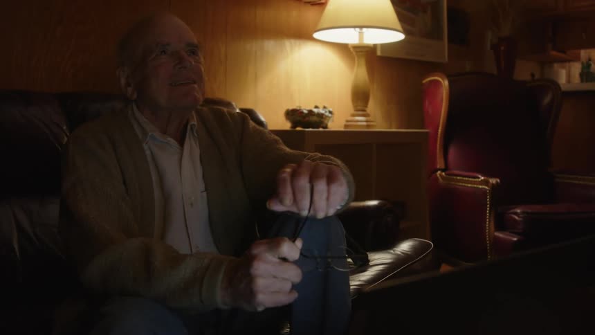 An older elderly man is sitting on the couch and on his laptop