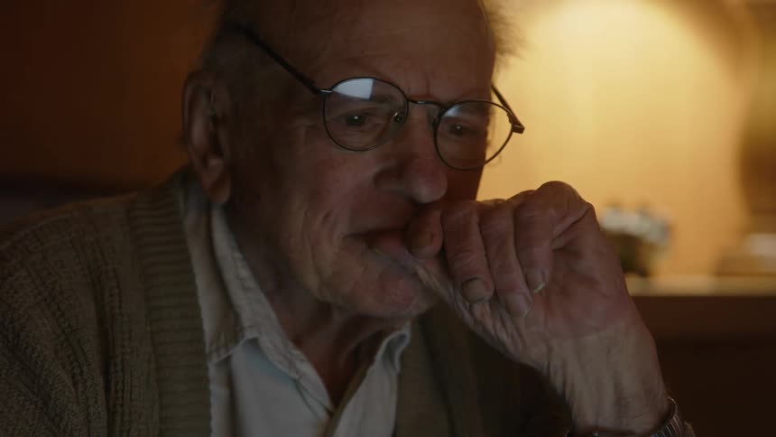 Elderly man sitting on a couch at home types on a laptop over the coffee table