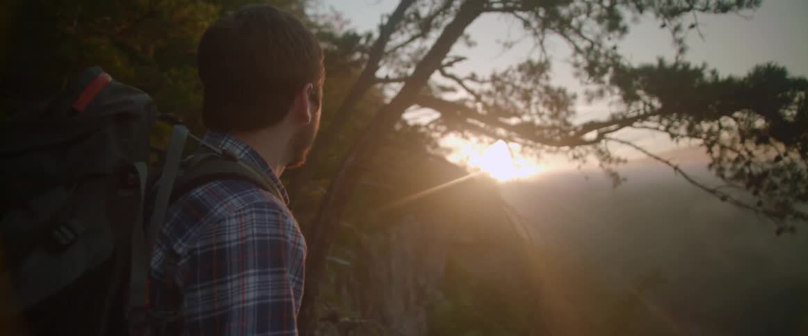 A man is standing outside overlooking the edge of a cliff at sunset