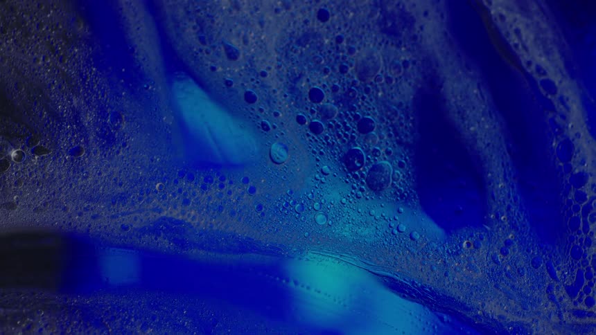 Close up of glass covered in soap bubbles in front of a bright blue background