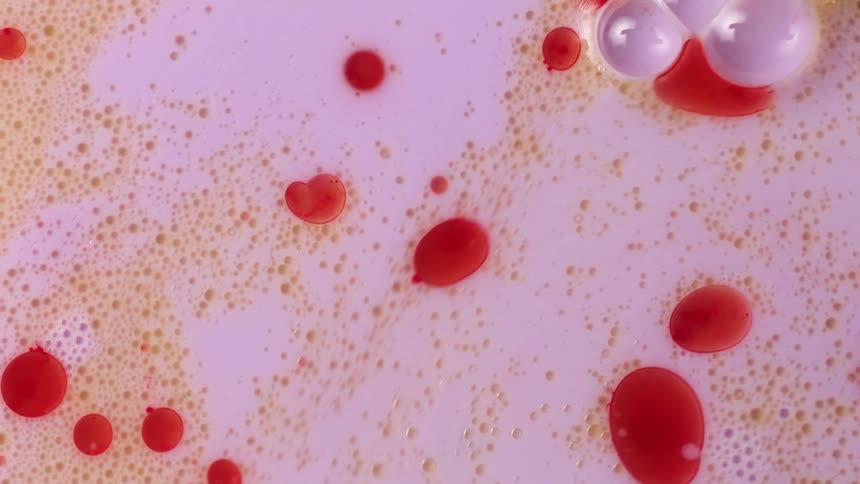 Red spheres are floating among small gold orbs in pink liquid as large pink bubbles move through and push the others away