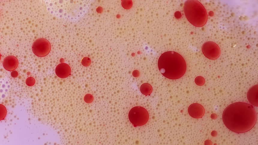 Red orbs float on a bubbly surface as a pink liquid ripples and moves