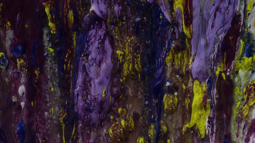 Close up of a chaotic mass of purple and yellow ink streaming down a vertical surface