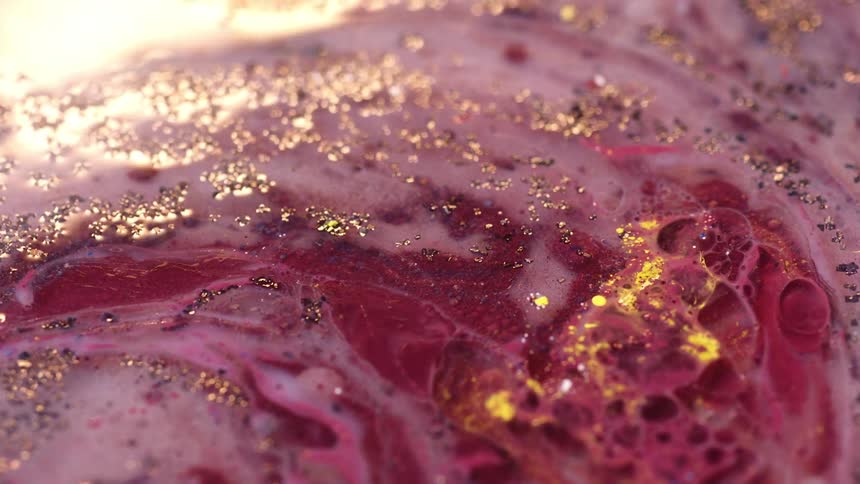 Pink and purple paint with bubbles and black particles in it with a orange reflection shining across it