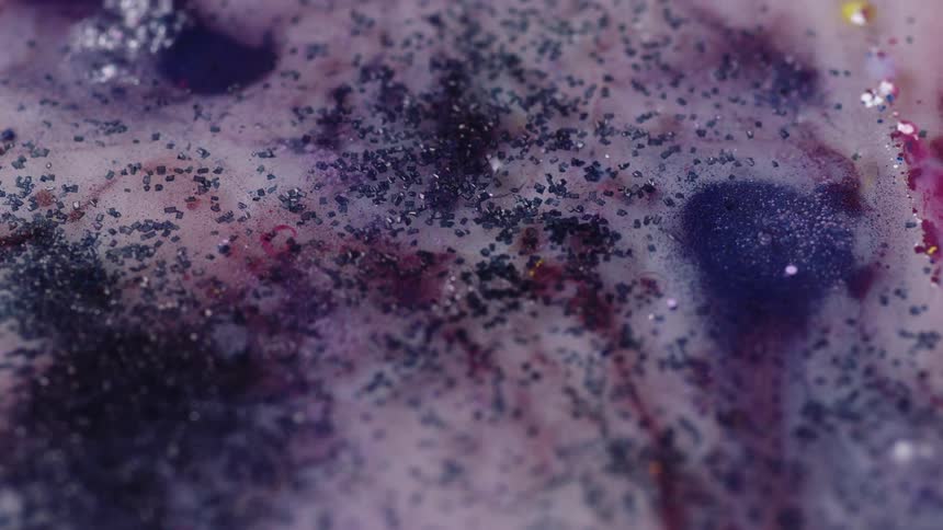 Close up of colorful inks mixed chaotically showered with blue glitter