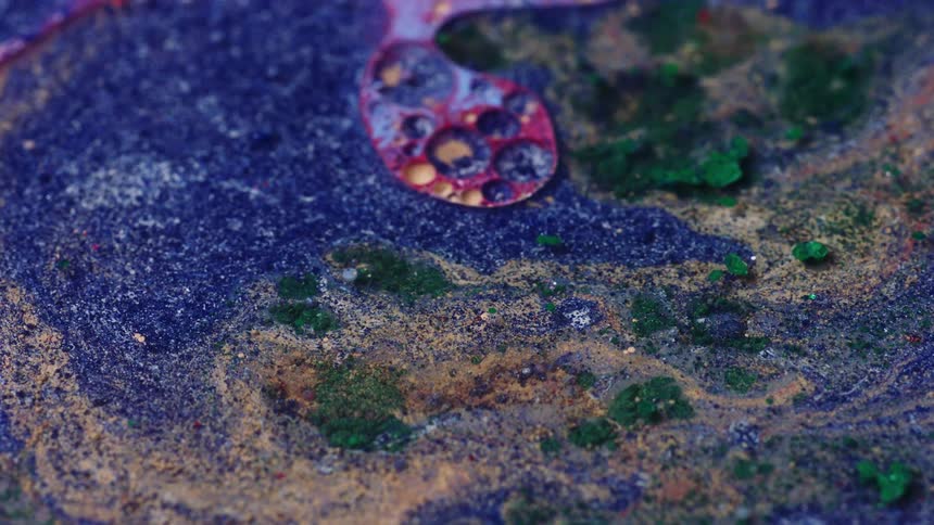 Close up of the chaotic surface of mixed liquid inks covered in glitter