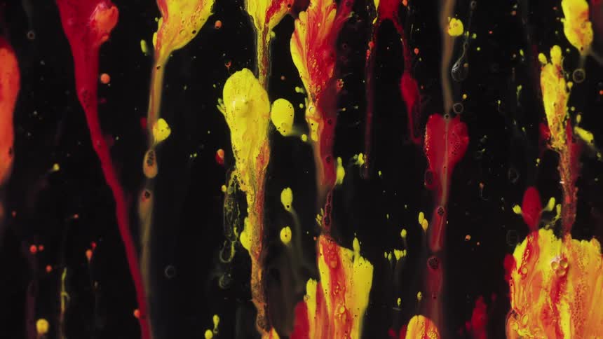 Red and yellow streaks are slowly moving and mixing as they drip in the darkness