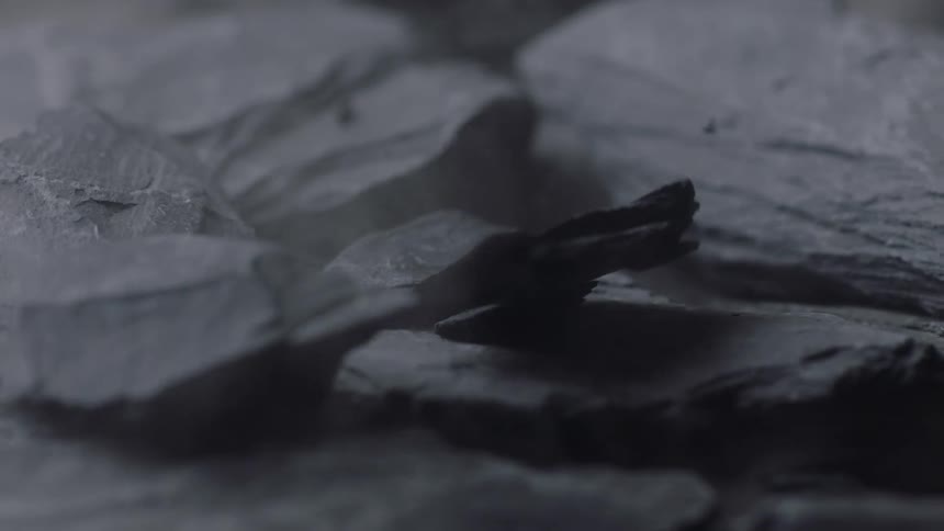 Pieces of jagged gray stone fall and tumble onto a pile of several other pieces