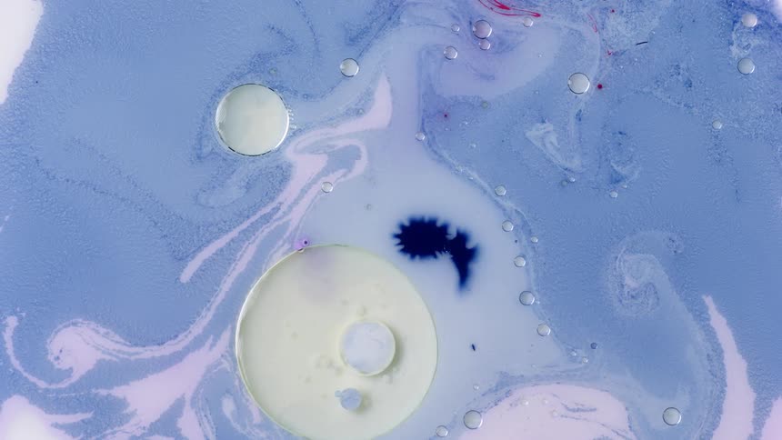 White orbs and bubbles float in a blue liquid with some pink mixing in