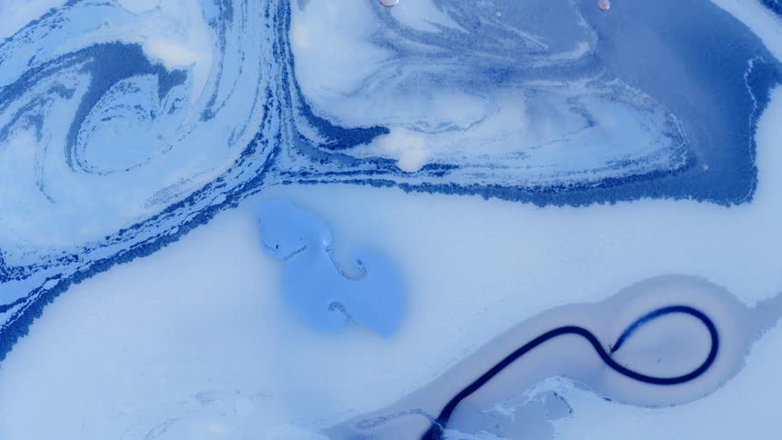 Blue lines swirl and blend as they stretch across the white liquid surface