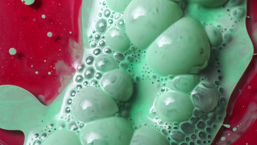 A colorful green liquid is poured atop a red liquid and generates a number of bubbles
