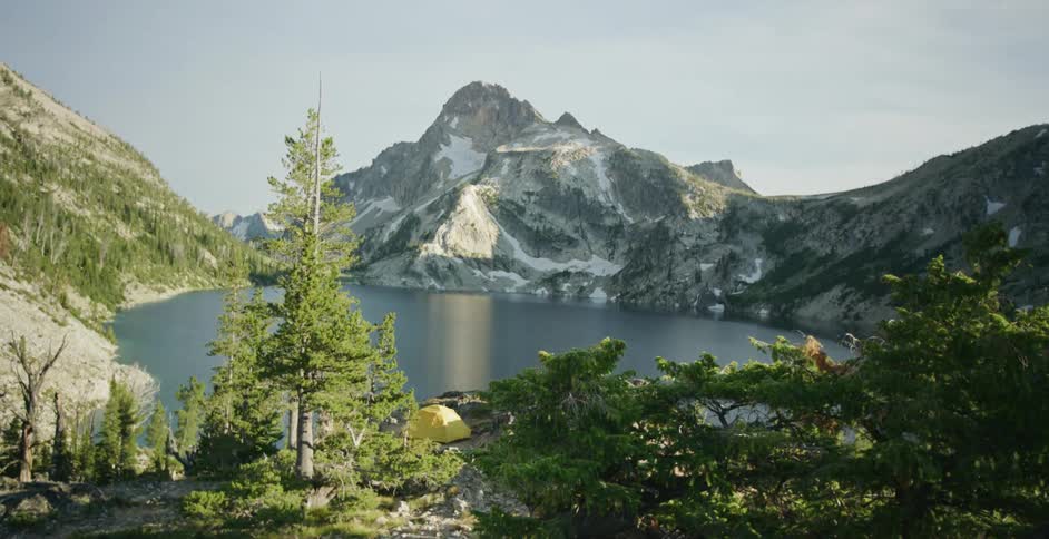 Yellow tent set up on the shores of a lake near the snow covered slopes of a mountain at morning