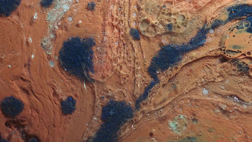 Top down close up of brown and blue blobs of ink under shifting lights